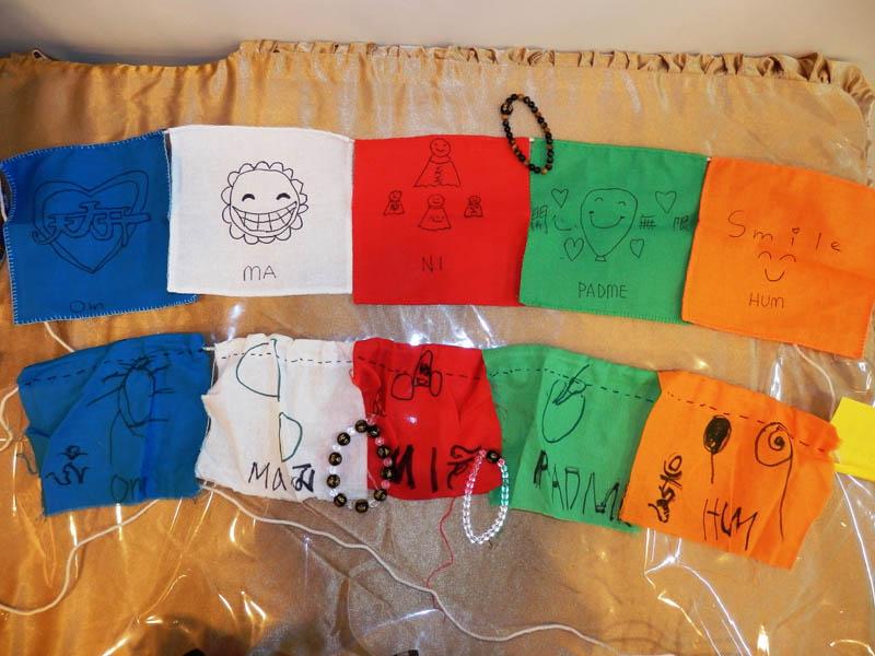 小朋友製作的風馬旗、念珠已經過大寶法王加持；上方風馬旗的繪畫者七歲半，下方的五歲，後者畫風明顯較簡單，但他依樣畫葫蘆地「繪」上了藏文六字大明咒。